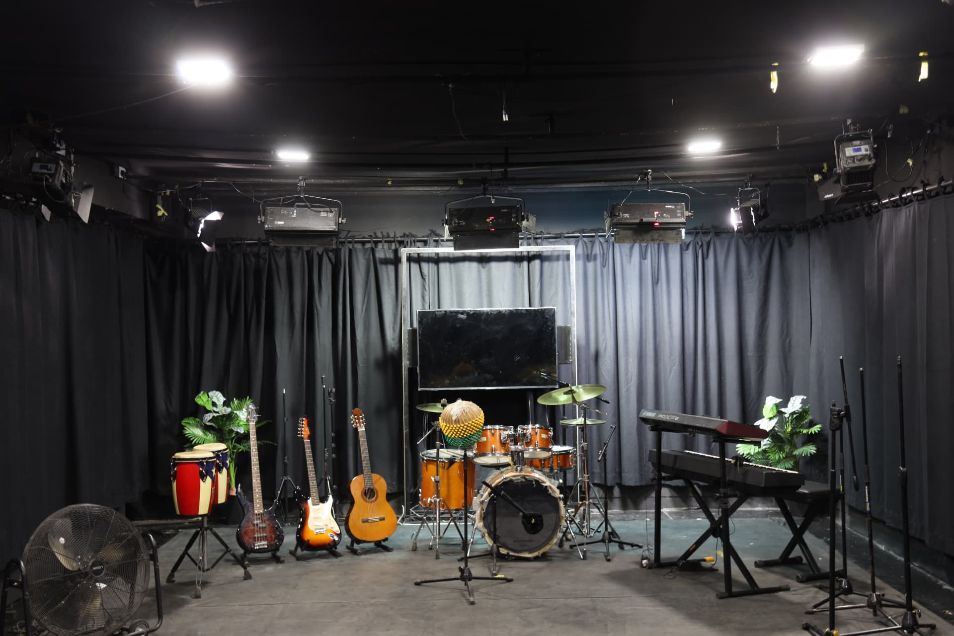 Wide centered view of the studio floor stage with full band instrumentation, overhead lights and mic stands