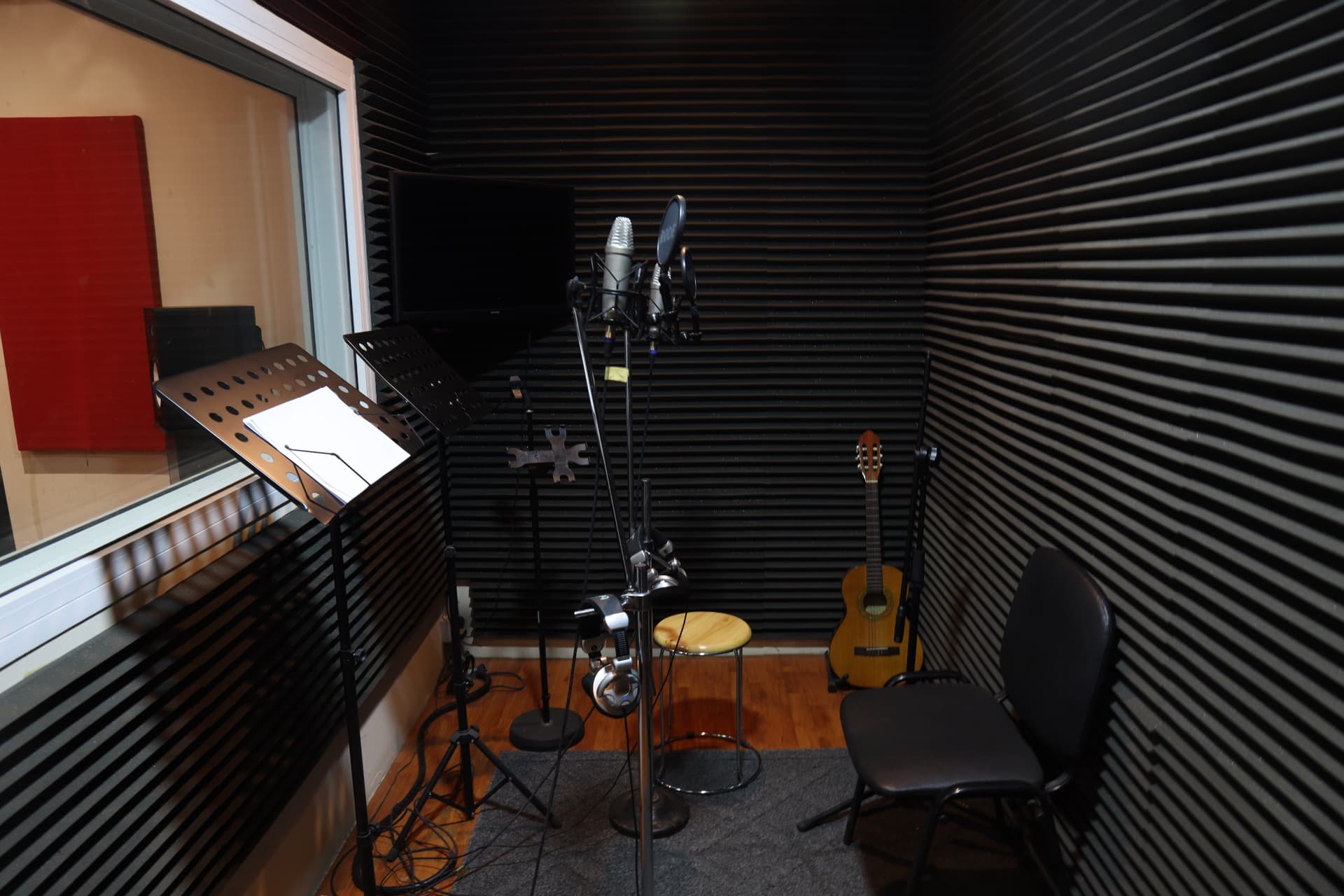 Vocal booth in Sound Suite 1 with microphones, pop filter, music stand and guitar against acoustic foam