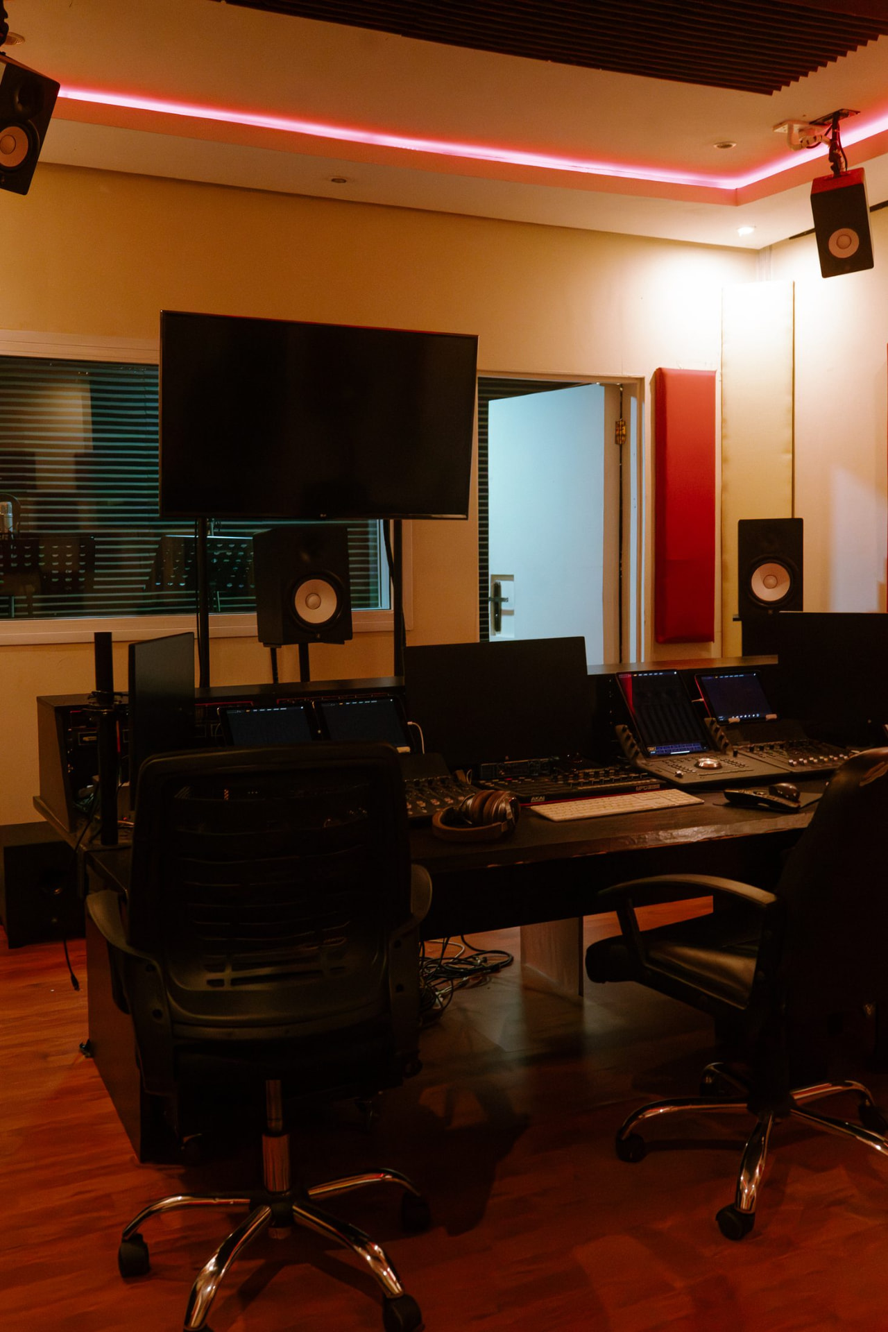 VFX and AI suite with red ambient lighting, mixing desk, dual control surfaces and wall display
